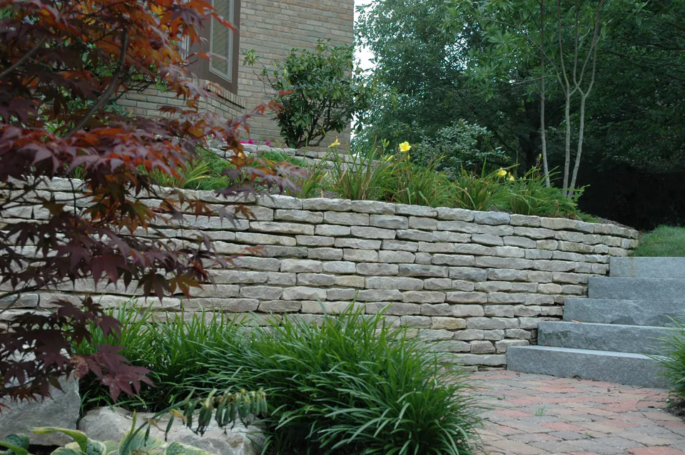 Dry-laid limestone retaining wall with stone steps and daylilies above a brick walk